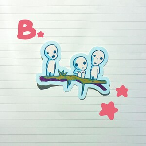 May include: A sticker featuring three small, white figures with large eyes, perched on a brown branch with green leaves. The sticker has a light blue outline and is accompanied by pink stars and the letter "B".