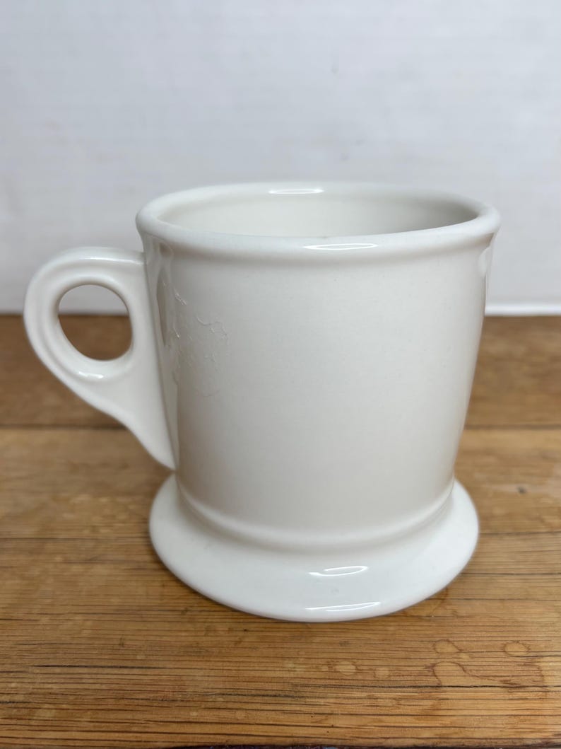 Pu&ograve; includere: Una tazza in ceramica bianca con base arrotondata e manico. La tazza ha un design semplice e classico ed &egrave; adatta per bevande calde. La tazza &egrave; su una superficie di legno.