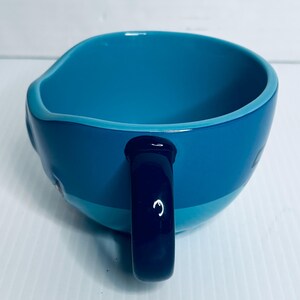 K&ouml;nnte beinhalten: Ein Keramikbecher mit zweifarbigem blauem Design, hellblauem Innenraum und dunkelblauer Au&szlig;enseite. Der Becher hat eine glatte, gl&auml;nzende Oberfl&auml;che und einen stabilen, dunkelblauen Henkel an der Seite, der eine schlichte Form aufweist.