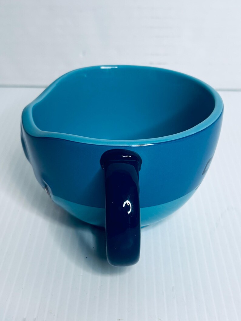 K&ouml;nnte beinhalten: Ein Keramikbecher mit zweifarbigem blauem Design, hellblauem Innenraum und dunkelblauer Au&szlig;enseite. Der Becher hat eine glatte, gl&auml;nzende Oberfl&auml;che und einen stabilen, dunkelblauen Henkel an der Seite, der eine schlichte Form aufweist.