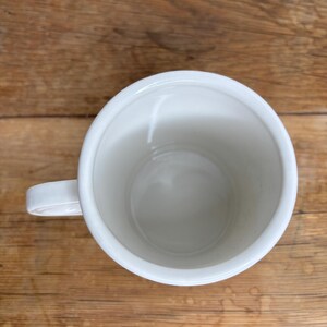 Pu&ograve; includere: Una tazza di ceramica bianca con manico. La tazza &egrave; vuota e si trova su una superficie di legno. La tazza &egrave; rotonda con una finitura liscia e lucida.