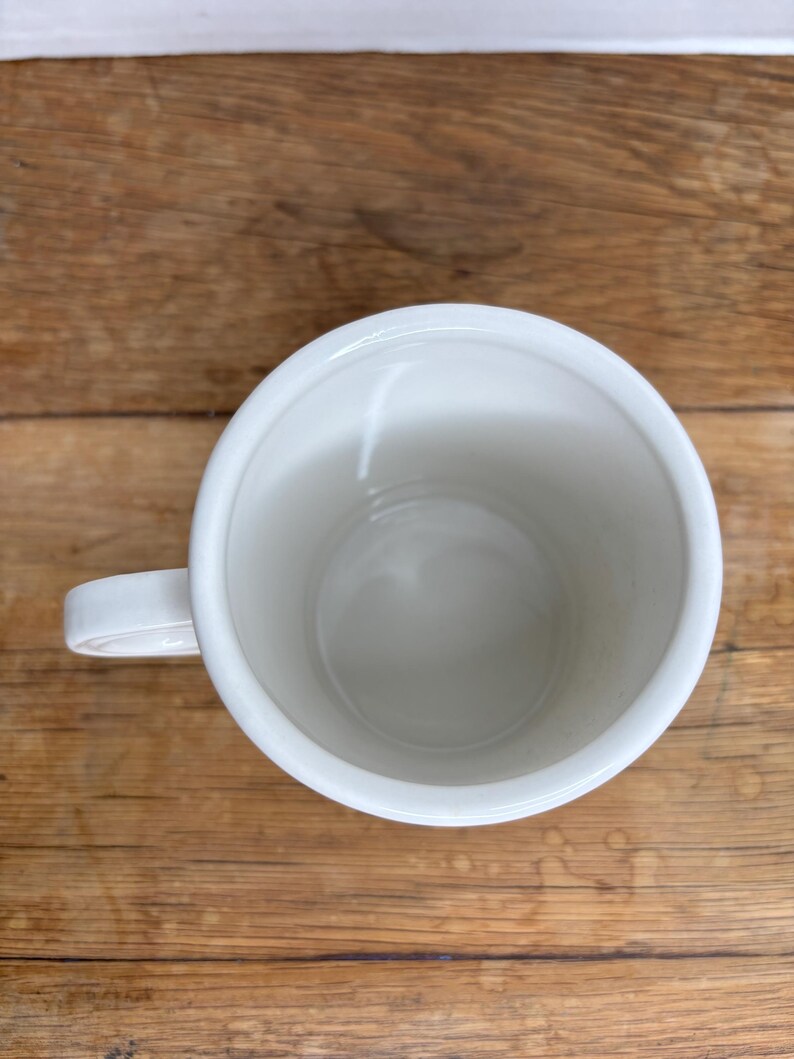 Pu&ograve; includere: Una tazza di ceramica bianca con manico. La tazza &egrave; vuota e si trova su una superficie di legno. La tazza &egrave; rotonda con una finitura liscia e lucida.