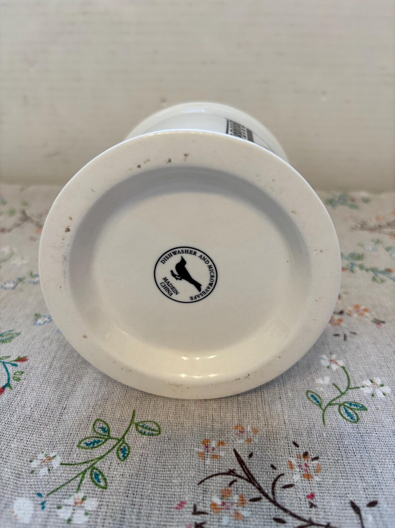 Puede incluir: Taza de cer&aacute;mica blanca con base ancha y parte superior ligeramente acampanada. La parte inferior de la taza presenta un sello en blanco y negro que dice "Apto para lavavajillas y microondas" y "Hecho en China".