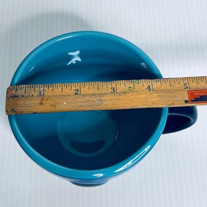 K&ouml;nnte beinhalten: Eine t&uuml;rkisfarbene Keramiktasse von oben betrachtet, mit einem Holzlineal &uuml;ber der &Ouml;ffnung. Das Lineal zeigt, dass die Tasse einen Durchmesser von etwa 12,7 cm hat. Das Innere der Tasse ist in einem einfarbigen, gl&auml;nzenden T&uuml;rkiston gehalten.