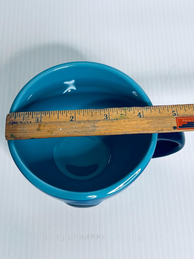 K&ouml;nnte beinhalten: Eine t&uuml;rkisfarbene Keramiktasse von oben betrachtet, mit einem Holzlineal &uuml;ber der &Ouml;ffnung. Das Lineal zeigt, dass die Tasse einen Durchmesser von etwa 12,7 cm hat. Das Innere der Tasse ist in einem einfarbigen, gl&auml;nzenden T&uuml;rkiston gehalten.