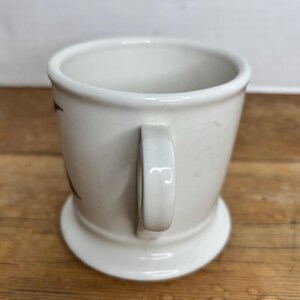 Pu&ograve; includere: Una tazza in ceramica bianca con base arrotondata e manico. La tazza ha un design semplice ed &egrave; appoggiata su una superficie di legno. La tazza &egrave; vuota e pronta per essere riempita con una bevanda.