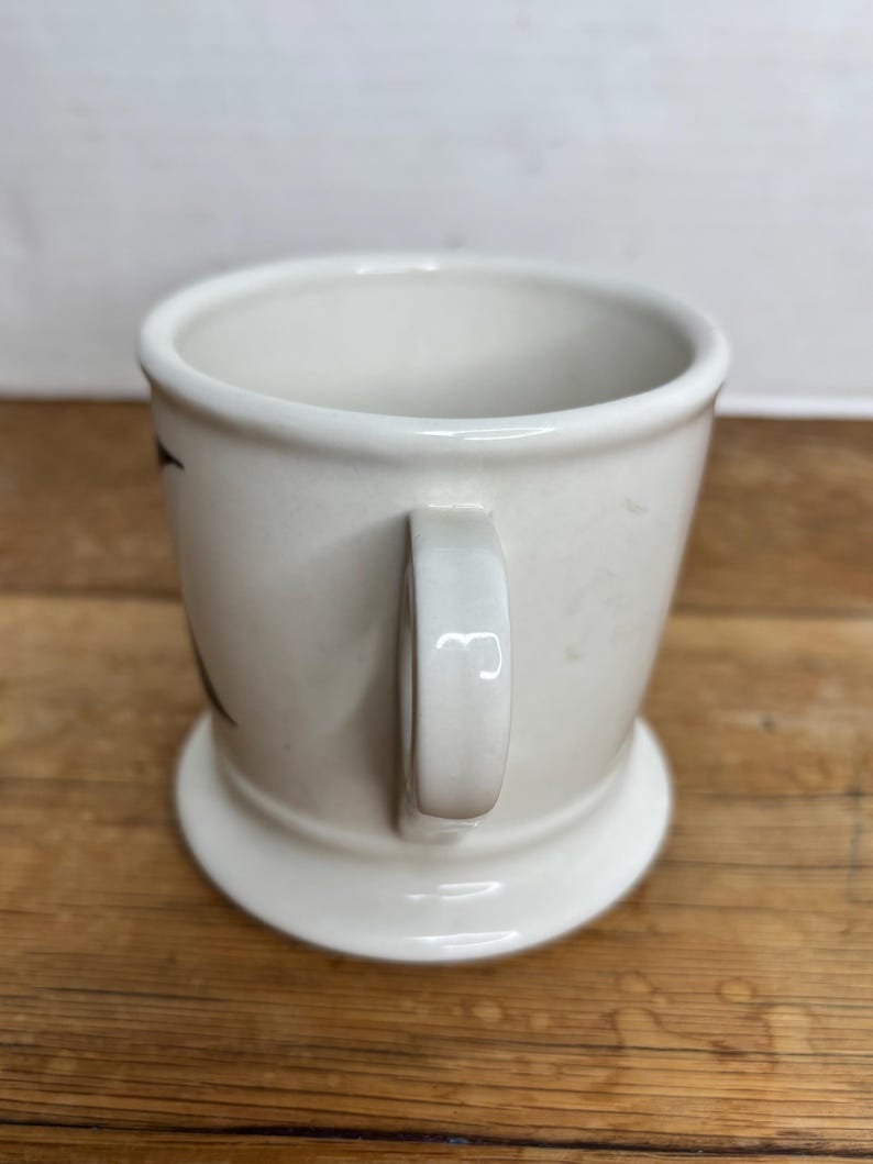Pu&ograve; includere: Una tazza in ceramica bianca con base arrotondata e manico. La tazza ha un design semplice ed &egrave; appoggiata su una superficie di legno. La tazza &egrave; vuota e pronta per essere riempita con una bevanda.