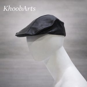 May include: A black leather flat cap. The cap is displayed on a white mannequin head. The text "KhoobArts" is in the upper left corner. The cap has a curved brim and a rounded crown.