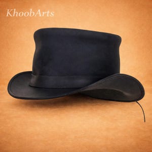 May include: A black top hat with a wide brim and a ribbon band. The hat is made of a dark material and has a classic, formal design. The text "KhoobArts" is in the top left corner.