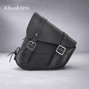 May include: Black leather motorcycle saddlebag with silver buckles and straps. The bag has a triangular shape with a flap closure and is designed to be mounted on a motorcycle. The brand name "KhoobArts" is visible in the upper left corner.