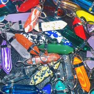 May include: A selection of gemstone pendants in a variety of colours, such as red, blue, green, and orange. Each pendant features a silver-coloured metal cap and loop. The gemstones display unique patterns and textures, creating a diverse assortment of jewellery.