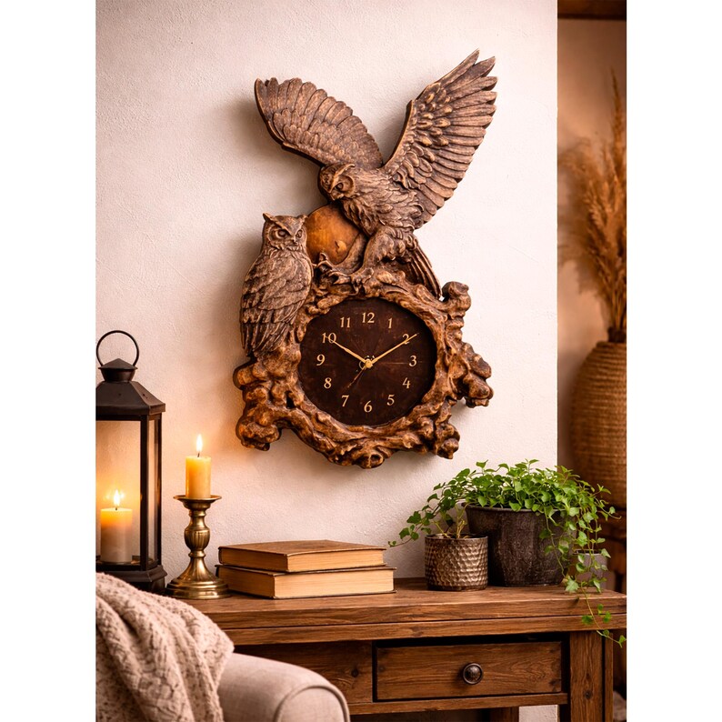 May include: A brown wall clock featuring a sculpted design of two owls, one perched and one with wings spread wide. The clock face is circular with gold-coloured hands and numerals, set within a textured, wood-like frame with organic, branch-like details.