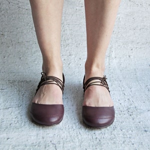 Może przedstawiać: Para brązowych skórzanych butów ze sznurówkami owiniętymi wokół kostek.