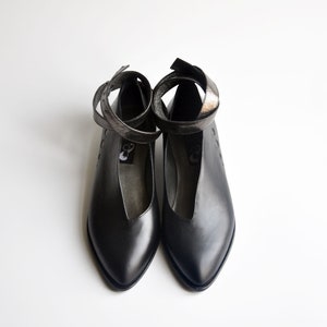 Może przedstawiać: Czarne skórzane buty ze spiczastym noskiem i paskami na kostkę. Paski są owinięte wokół kostki i zawiązane na kokardkę z przodu.