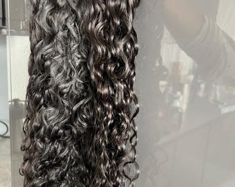 Pode incluir: Extensões de cabelo encaracolado castanho escuro. O cabelo é muito encaracolado e parece ser de cor natural. Uma etiqueta com as letras "LL" e o endereço do site www.luxlayers.co.uk está presa ao cabelo.