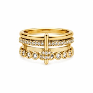 Puede incluir: Un conjunto de cuatro anillos dorados. Uno es una banda lisa, otro está incrustado con pequeñas piedras preciosas transparentes, y un tercero presenta piedras preciosas transparentes más grandes. Un cuarto anillo tiene una barra vertical con un grupo de piedras preciosas.