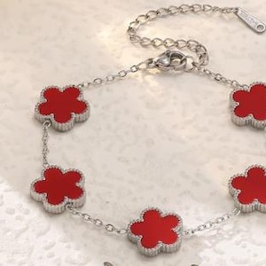 May include: Silver-toned bracelet featuring five red flower-shaped charms. The charms are evenly spaced along a delicate chain. The bracelet has an adjustable length and a secure clasp. The design is simple yet elegant, suitable for everyday wear.