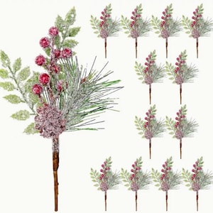 May include: Artificial Christmas floral picks featuring red berries, green pine needles, and frosted leaves. The picks have a brown stem and a frosted, glittery finish, perfect for holiday decorations.