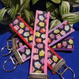 May include: Four colorful keychains with a black background and a pattern of owls in various colors. The keychains have silver key rings and are attached to a silver swivel clasp.
