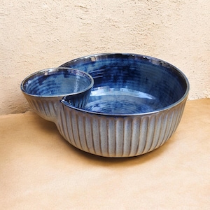 May include: A two-part ceramic serving bowl with a deep blue glaze. The larger bowl has vertical ribbed detailing, and a smaller bowl is attached. The bowls are ideal for serving snacks or dips.