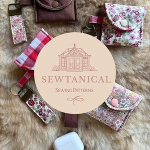 Può includere: Un assortimento di piccole pochette e portachiavi in tessuto di vari colori e fantasie. Alcune pochette sono marroni tinta unita, mentre altre presentano stampe floreali e a quadri. I portachiavi hanno disegni in tessuto coordinati. È visibile anche una custodia bianca per AirPod.