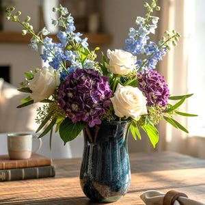May include: A floral arrangement featuring purple hydrangea blooms, white roses, and tall light blue delphinium stems. The flowers are displayed in a dark blue, glossy ceramic vase with a tapered neck and a rounded base, creating a vibrant centerpiece.