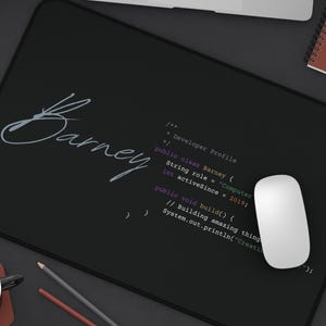 May include: Black rectangular mousepad with the name "Barney" in cursive script. The mousepad also features computer code and a white mouse. A laptop, notebook, and coffee cup are also visible.