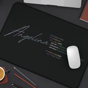 May include: Black rectangular mousepad with the name "Angelina" in white script. The mousepad also features a developer profile with coding text and a white computer mouse. A laptop, notebook, and coffee cup are also visible.