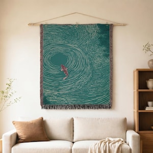 May include: A rectangular woven wall tapestry featuring a deep teal background with white concentric circular patterns resembling water ripples and a single red koi fish swimming in the center. The tapestry has a fringed edge and is hung.