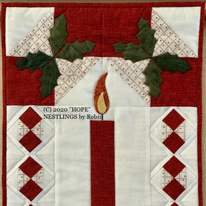 May include: A red, white, and green quilted wall hanging with a red candle in the center. The candle is surrounded by a wreath of green holly leaves. The text "(C) 2020 "HOPE" NESTLINGS by Robin" is printed at the top of the hanging.