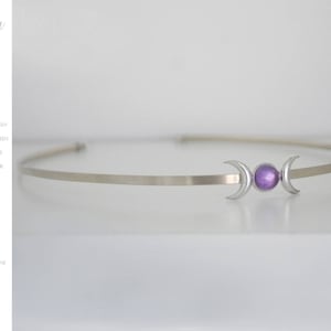 Pode incluir: Um colar choker de prata com uma lua tripla e uma pedra preciosa roxa no centro.