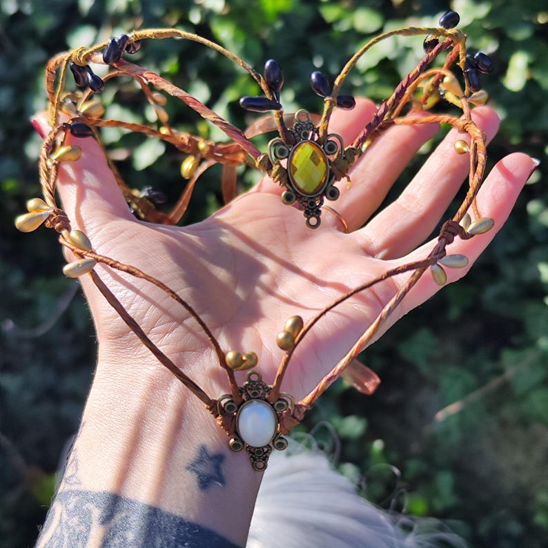 Puede incluir: Una diadema delicada, de color marr&oacute;n, con forma de rama, con detalles dorados y negros. La diadema presenta dos piedras preciosas ovaladas, una amarilla y otra blanca.
