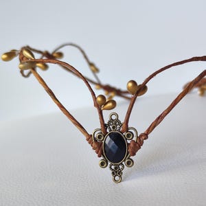 Puede incluir: Una corona de ramas marrones con detalles dorados y una piedra preciosa negra en un engaste de bronce.