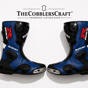 Peut inclure: Une paire de bottes de moto bleues et noires avec le logo Suzuki et la marque GSX en rouge et blanc. Les bottes comprennent des panneaux de protection noirs, des curseurs d'orteils argentés et des zones flexibles. Le texte THECOBBLERSCRAFT est visible.