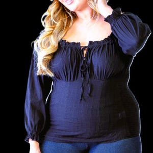 May include: A black long-sleeve top with a square neckline and a tie-up detail. The top has a fitted bodice and is paired with blue jeans. The sleeves have a ruffled cuff. The model has blonde hair.
