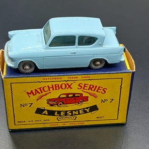 May include: A light blue Matchbox Series No. 7 toy car, atop its original yellow and blue box. The box features a red car illustration and the text "A Lesney Product". The toy car is a vintage collectible.