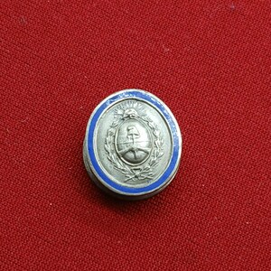 Può includere: Un bottone circolare in metallo color argento con un emblema centrale in rilievo raffigurante un berretto frigio su un'asta circondato da una corona d'alloro, il tutto racchiuso da un sottile bordo in smalto blu.