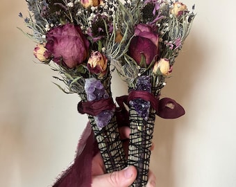 May include: Two bundles of dried flowers and herbs, including deep red roses, lavender, and baby's breath, are tied with black string. Each bundle features a raw purple amethyst crystal attached with a dark burgundy ribbon tied in a bow.