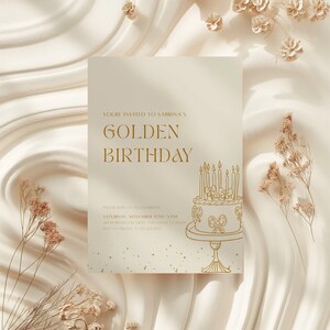 May include: A cream-colored invitation with gold text that reads "Golden Birthday." The invitation features a cake illustration with lit candles and decorative elements. The background is a soft, textured fabric.