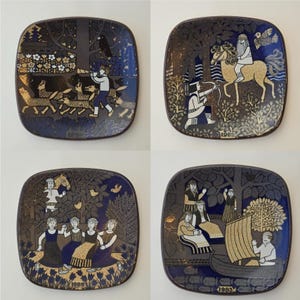 May include: Four square decorative plates with rounded corners. Each plate features a different scene with figures, animals, and trees in gold, white, and blue on a dark background. The plates have the years 1978, 1982, 1980, and 1983 printed on them.