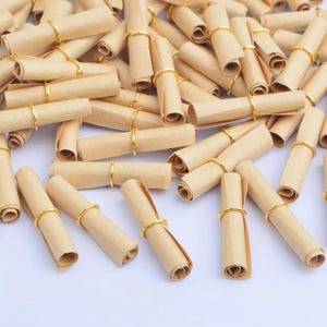 May include: A large collection of small, tightly rolled scrolls made from light brown paper. Each individual scroll is secured in the center with a thin, shiny gold-colored metal ring, creating a uniform appearance across the entire group.