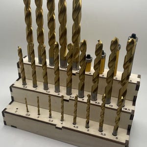 以下が含まれることがあります： さまざまなサイズの金色のドリルビットのセットが入った、木製の段々になったオーガナイザー。サイズはミリメートルで表示され、2から10.5まであります。ドリルビットは階段状に配置されており、最も小さいものが前面にあります。