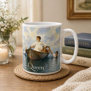 Puede incluir: Una taza de cerámica blanca con una ilustración impresa de una persona con vestido blanco sentada en un bote de remos de madera sobre el agua, con otra persona nadando al lado. La palabra Queen está impresa en blanco en la parte inferior.