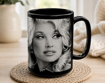 May include: A black ceramic mug featuring a high-contrast, black and white photographic portrait of a person with voluminous blonde hair and hoop earrings. The mug has a smooth, glossy finish and a curved handle on the right side for easy gripping.