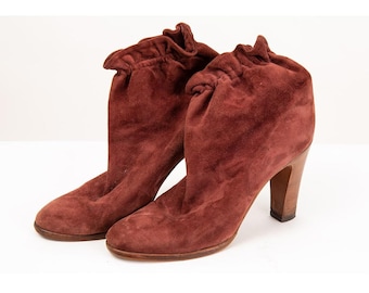 May include: A pair of burgundy suede ankle boots with a gathered detail at the top of the shaft and a block heel.
