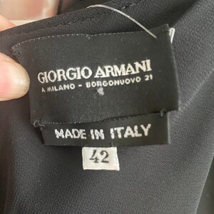 May include: Black label with white text that reads "Giorgio Armani A Milano - Borgonuvo 21" and "Made in Italy". A white tag with the number "42" is attached to the label.