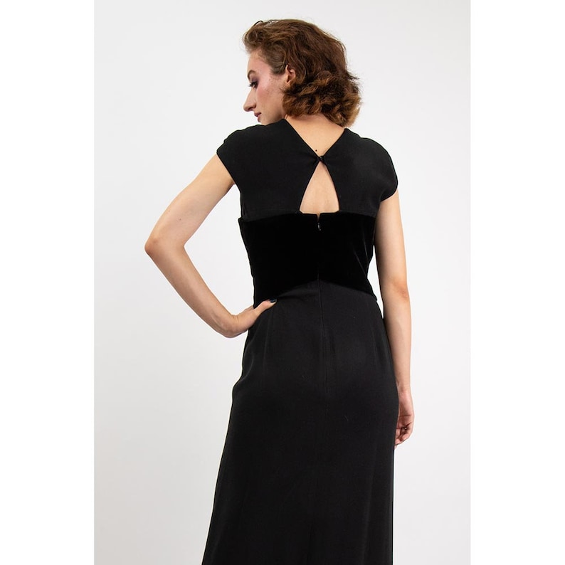 May include: A black sleeveless dress with a velvet bodice and a keyhole back. The dress has a simple, elegant design.