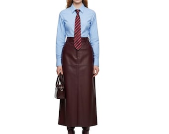 May include: A woman wearing a light blue button-down shirt, a burgundy striped tie, and a long burgundy leather skirt. She is also wearing burgundy boots and carrying a small burgundy handbag. The outfit is a mix of classic and modern styles.