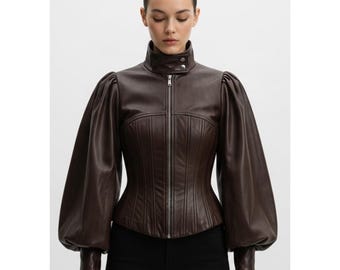 May include: A brown leather jacket with a high collar and a zip-up front. The jacket features long, voluminous sleeves and a fitted bodice. The model is wearing black pants. The jacket's design is a blend of classic and modern styles.