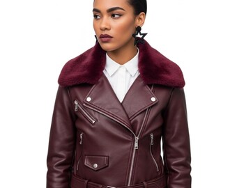 May include: A burgundy faux leather motorcycle jacket with a faux fur collar. The jacket features a belted waist, multiple zippered pockets, and silver hardware. The model is wearing a white collared shirt underneath.